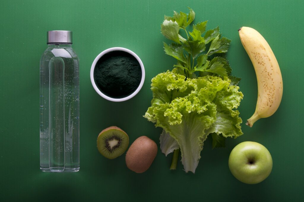 Ingrediënten voor voeding en ontspanning: fles water, spirulina, sla, selderij, kiwi, banaan en groene appel