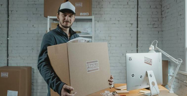 Man tilt een grote verhuisdoos met label 'fragile' in een kantooromgeving – verhuisdozen tillen